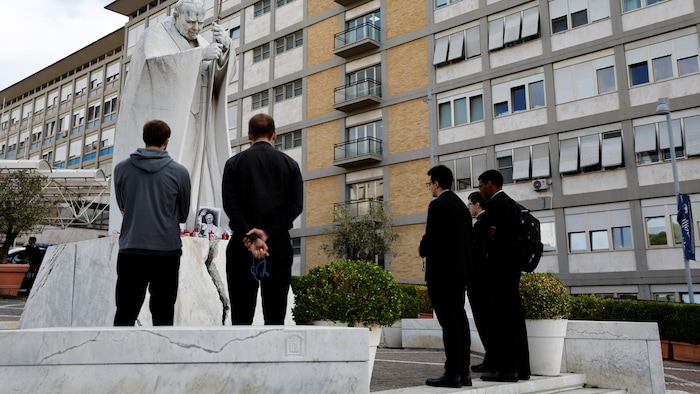 Des prêtres et des fidèles prient le rosaire devant la statue du défunt pape Jean-Paul II, à l'extérieur de l'hôpital Gemelli, après que le Vatican a annoncé que l'état de santé du pape s'améliorait progressivement et qu'il ferait sa première apparition publique depuis son hospitalisation dimanche pour prononcer la prière traditionnelle de l'Angélus.