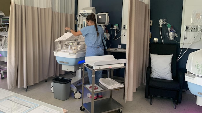 Une infirmière, de dos, devant un incubateur.
