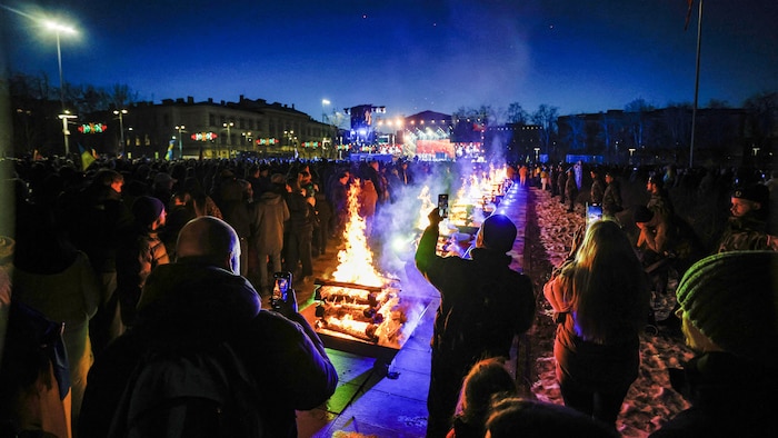 Des centaines de personnes regardent des feux brûler dans la pénombre.