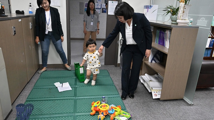 Une femme tient un enfant par la main et l'emmène dans une aire de jeux aménagée dans un bureau.