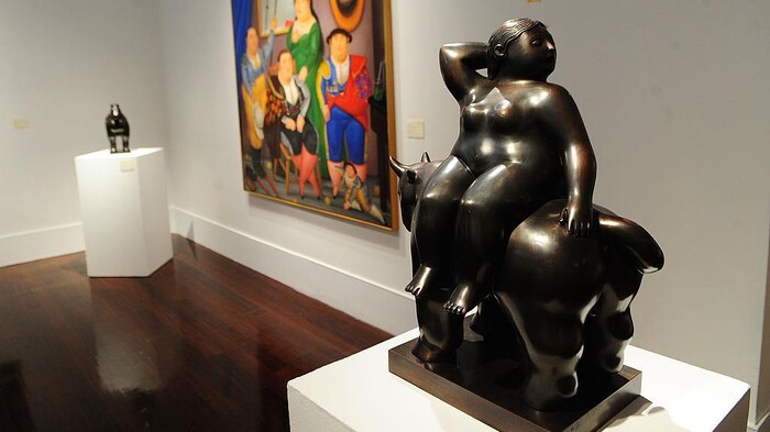 La sculpture de couleur foncée représente une femme assise sur un animal. 
