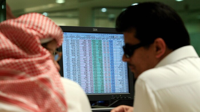 Des courtiers saoudiens discutent devant un écran qui affiche des titres boursiers.
