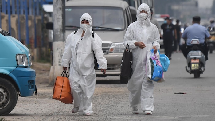 Deux femmes avec une combinaison blanche de protection marchent dans la rue à Pékin. 