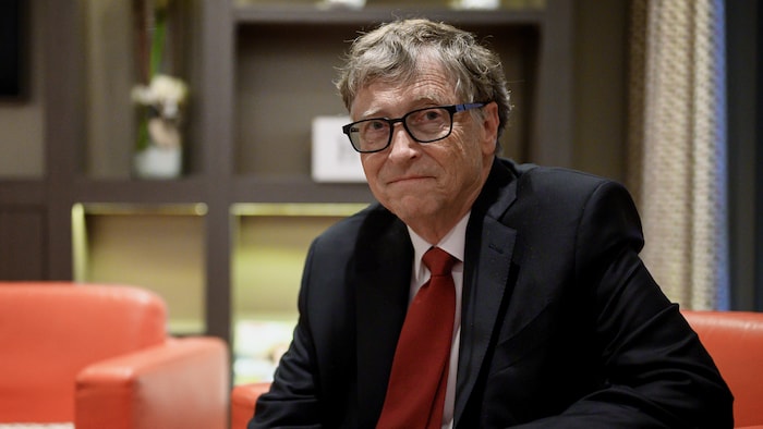 Bill Gates, assis sur un divan, regarde la caméra. 