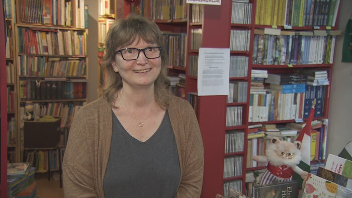 Une femme portant des lunettes devant des étagères de livres.