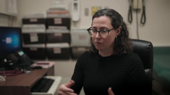 Une femme avec des lunettes est assise à son bureau. 