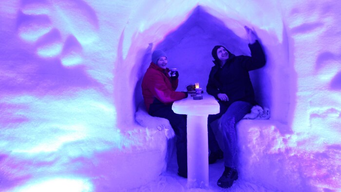 Une femme et un homme sont attablés dans un bâtiment fait de neige et de glace. 
