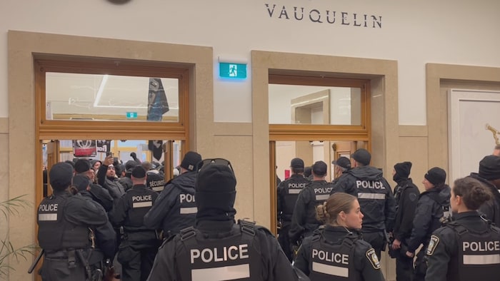Des policiers gardent les portes, derrière lesquelles ont voit des manifestants.