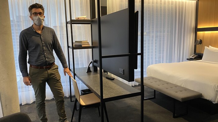 Un homme pose dans une chambre d'hôtel qui peut maintenant servir pour le télétravail.