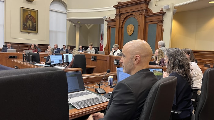 Desmarais fait dos à la caméra. Devant lui, des élus réunis à l'hôtel de ville.