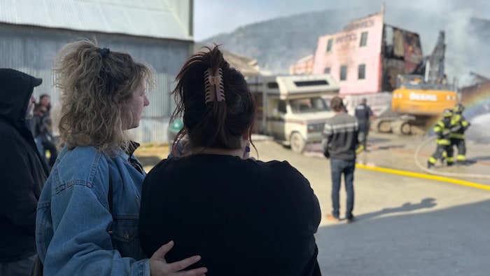 Des gens observnet un bâtiment en proie aux flammes autour duquel des pompiers s'activent.