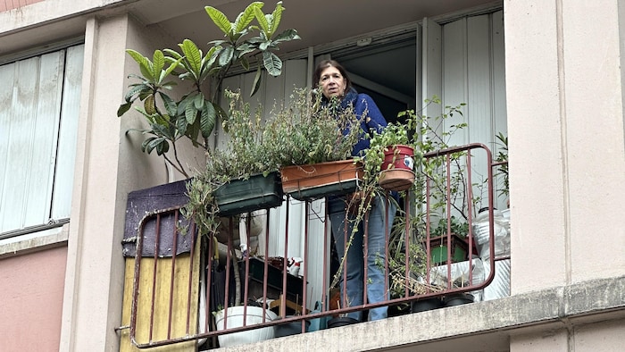 Une femme derrière des plantes sur un balcon.