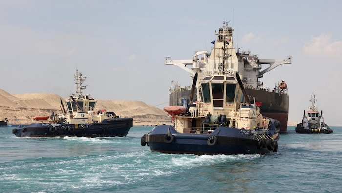 Trois bateaux remorquent un grand navire.
