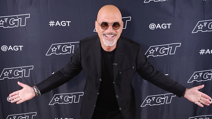 Howie Mendel sourit, les bras expansive ouverts, sur un tapis rouge de « America's Got Talent ».