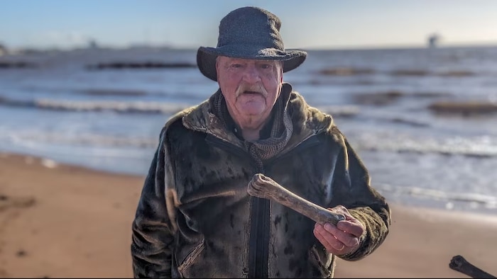 Ron House, sur la plage, tient un os dans sa main.