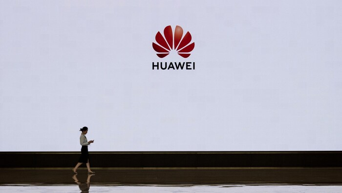 Une femme marche devant un écran blanc sur lequel est projeté le logo de la compagnie Huawei.