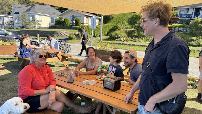 Il parle avec un groupe de gens assis à une table à pique-nique.