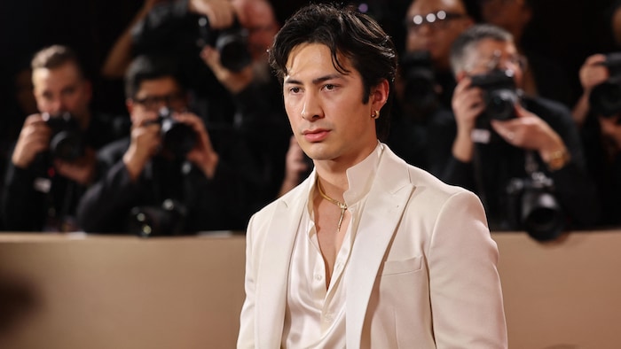 Un homme habillé en blanc pose sur le tapis rouge.