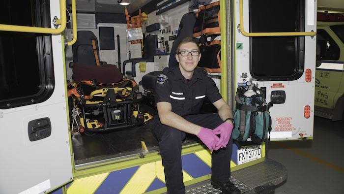 Hugo St-Onge, in uniform, sits on the first step behind the ambulance.