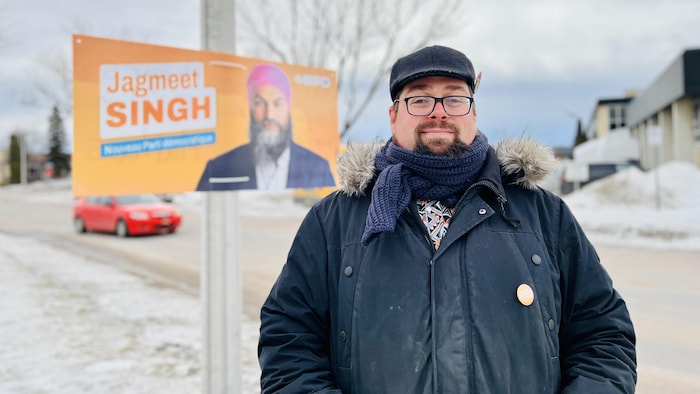 Un homme debout devant une pancarte.