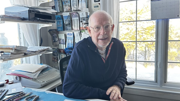 Portrait du propriétaire de Voyages Azur Rimouski, Hugues Langlois, assis derrière son bureau de travail à l'agence. 