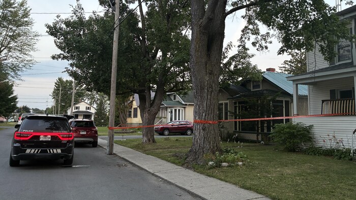 Un véhicule de police est immobilisé devant une résidence, entourée d'un ruban orange.