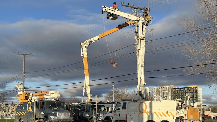 Des techniciens dans une nacelle travaillent près d'un poteau électrique.