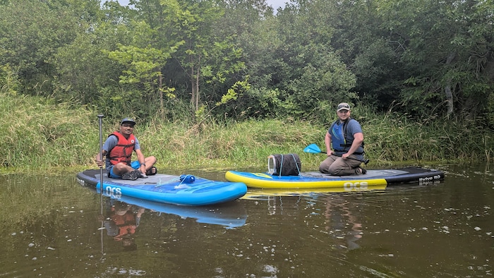 Akib Hasan et William Vincent sont assis sur leur planche à pagaie devant un site d'Hydrocharide grenouillette.