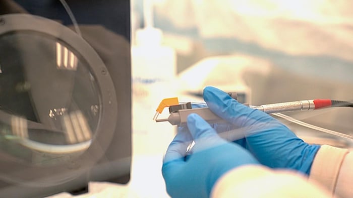 Gros plan sur des mains gantées de bleu manipulant le stylo-laser chirurgical innovant à côté d’un appareil de mesure dans un laboratoire médical.