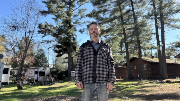 Portrait de Ian Foster au beau milieu de son parc portant un chandail à capuchon à carreaux et une paire de jeans.