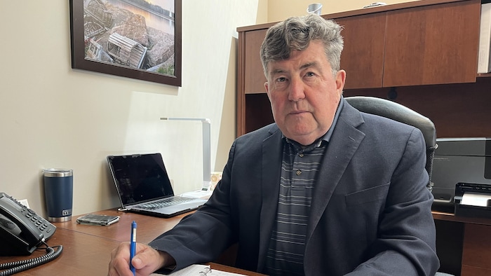 Ian Macpherson is sitting at his office. He holds a pen in his right hand. He looks at the camera.