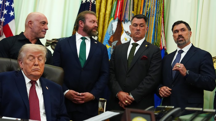 Donald Trump assit dans le bureau ovale avec Joe Rogan et trois autres dignitaires derrière lui.