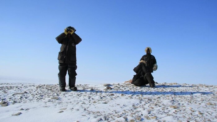 Three men on a snowy hill looking in binoculars.