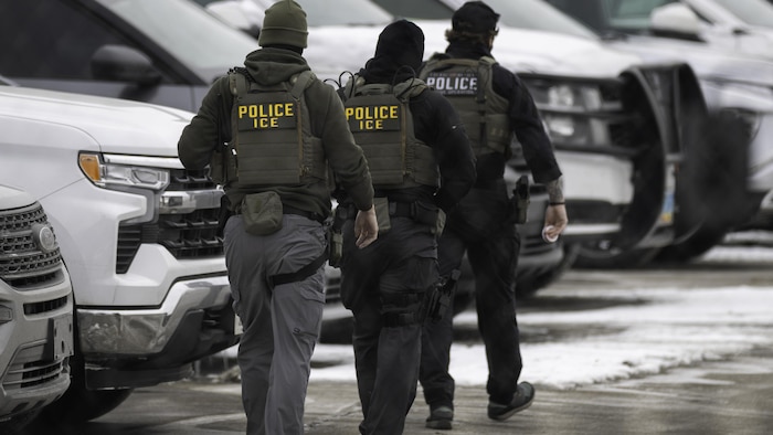 Trois agents de l'ICE marchent dans un stationnement.