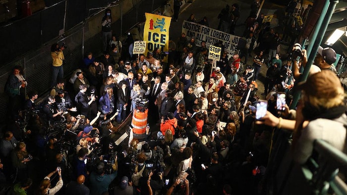 Une personne parle au micro au milieu d'élus, de caméramans, et de manifestants.