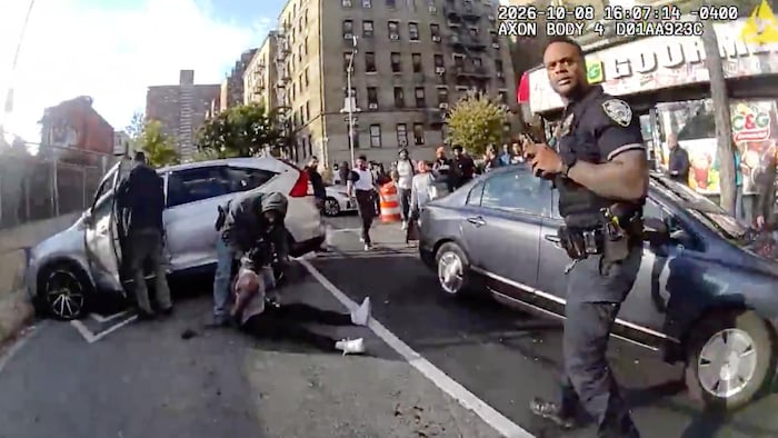 Un policier en uniforme s'approche d'un homme armé en tenue civile qui est penché vers un autre homme assis par terre, les mains liées dans le dos.