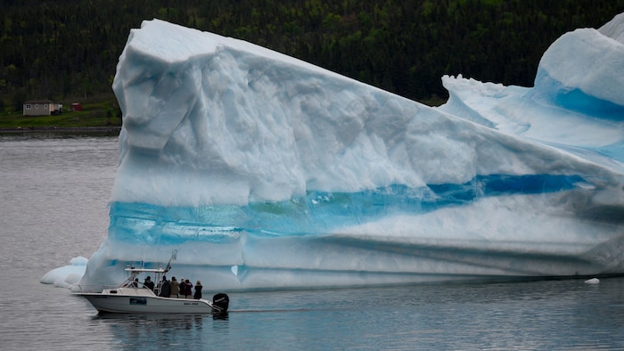 Quelques touristes à bord d'un bateau qui passe devant un iceberg.
