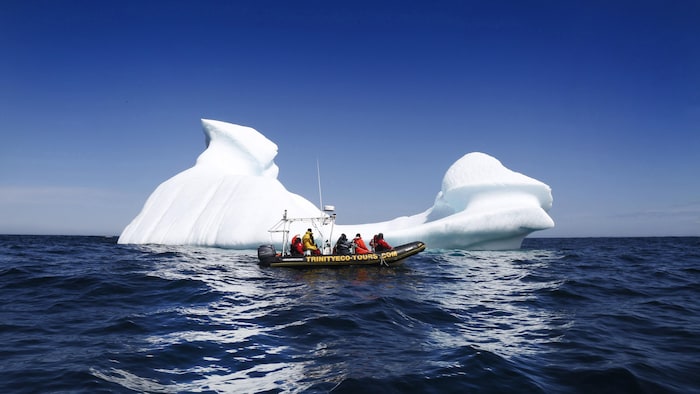 Des touristes sur un canot pneumatique devant un iceberg.