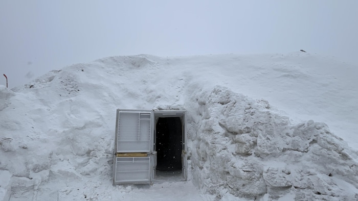 Une porte ouverte est installée dans une grande butte de neige.