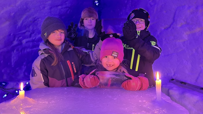 Quatre enfants sourient à la caméra dans un abri de neige.