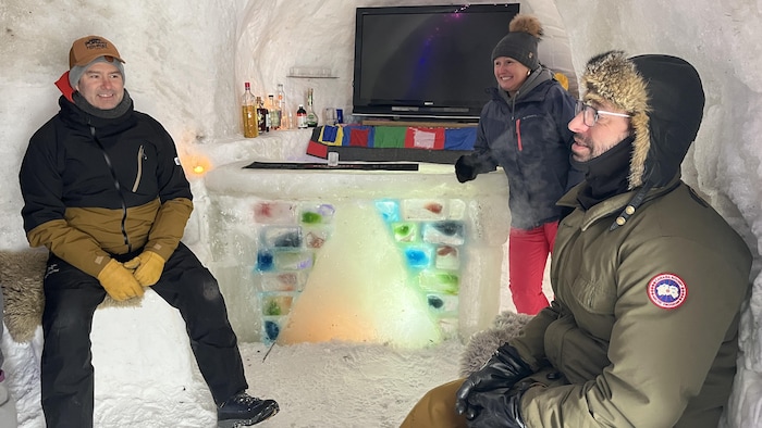 Trois adultes à l'intérieur d'un abri de neige sourient.