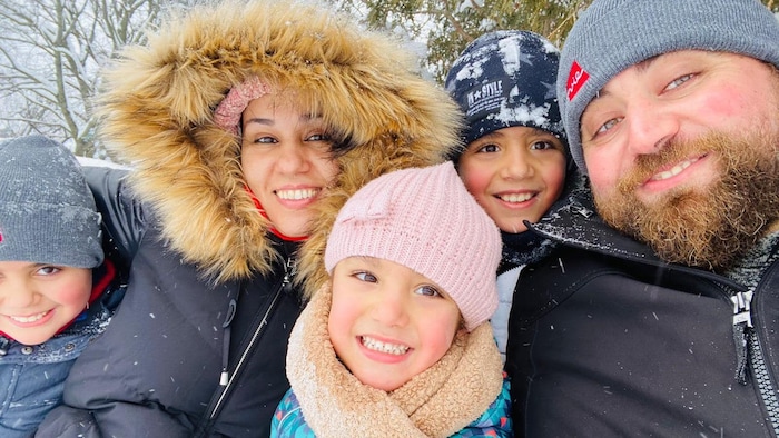 Ikram Khaouani, son mari et ses trois enfants sourient habillés de vêtements d'hiver à l'extérieur.