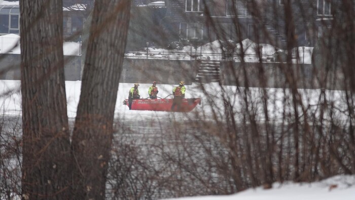 Trois secouristes autour d'une chaloupe sur la glace de la rivière des Prairies.