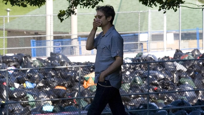 Un homme couvre son nez et sa bouche en marchant devant une montagne de sacs à ordures empilés dans la patinoire extérieure du parc Christie Pits, en juillet 2009.