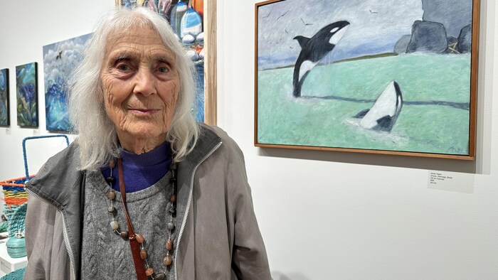 Anne Ngan devant sa peinture exposée lors du Herring Fest. Celle-ci représente des orques dans une mer turquoise.