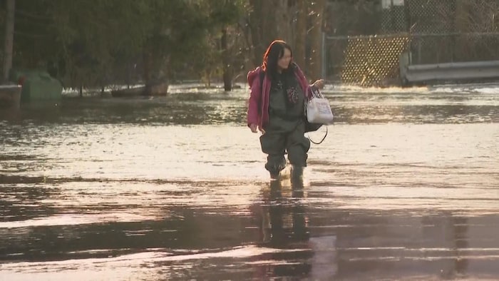 Une femme portant des bottes et un pantalon de pêche traverse une zone inondée.