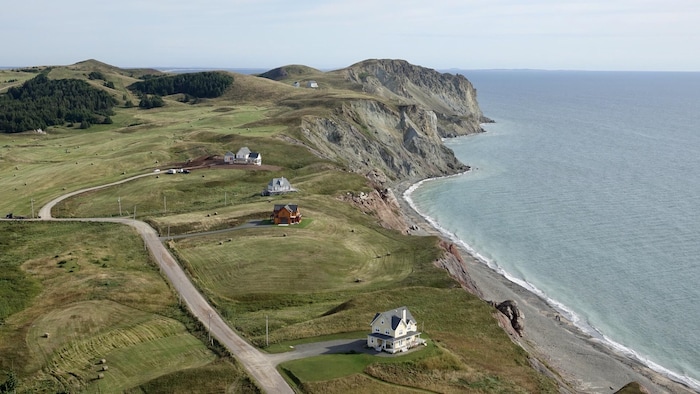 Vue sur des maisons neuves entourées de balles de foin devant des falaises de Havre-aux-Maisons.