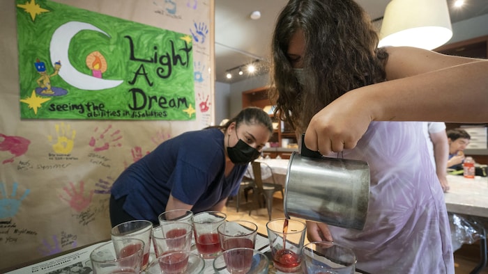 Une jeune femme en regarde une autre remplir des bougeoirs d'un liquide coloré.