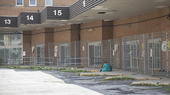 Une personne est assise par terre à l’arrière du bâtiment de l’Îlot Voyageur à Montréal.