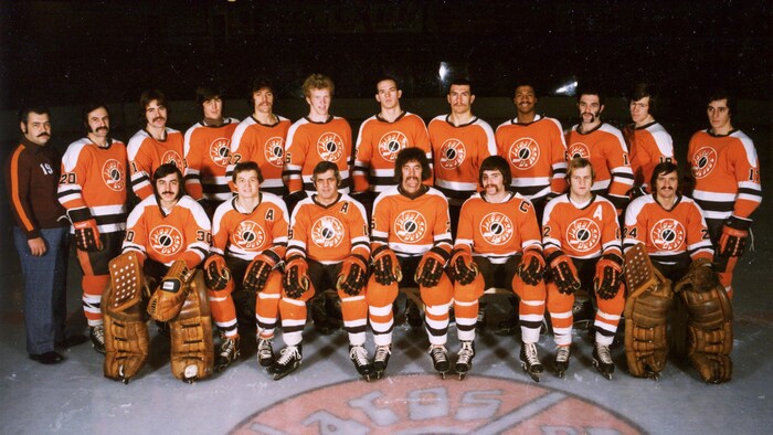 Photo d'équipe de hockey d'époque. Les joueurs sont alignés sur la glace, vêtus de leur uniforme orange, blanc et noir des Jaros de la Beauce.